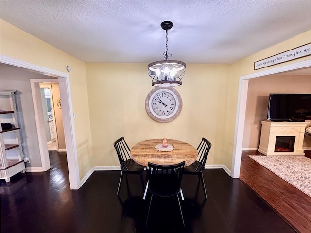 dining space featuring a textured ceiling, a notable chandelier, a fireplace, baseboards, and dark wood-style floors