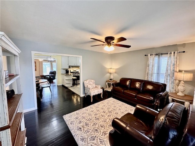 living area featuring ceiling fan with notable chandelier, dark wood-style flooring, and baseboards