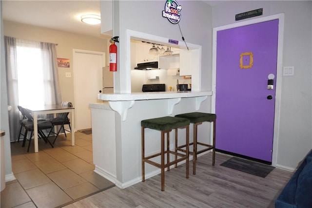 kitchen featuring light countertops, freestanding refrigerator, white cabinetry, a peninsula, and a kitchen breakfast bar