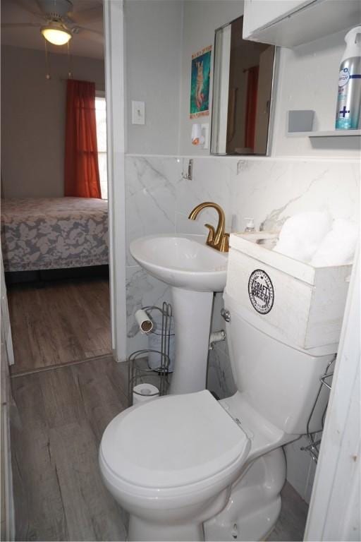 bathroom featuring tile walls, toilet, a sink, ensuite bath, and wood finished floors