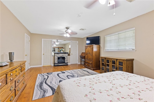 bedroom featuring ceiling fan, light hardwood / wood-style flooring, and a stone fireplace