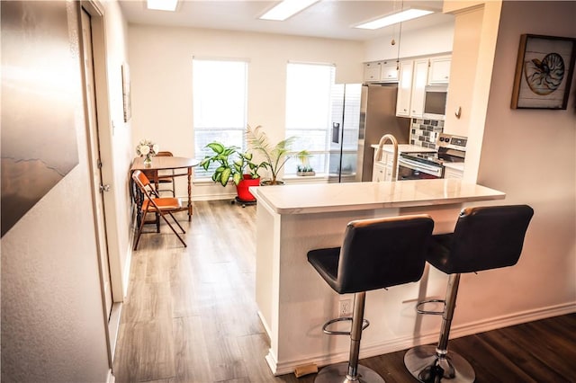 kitchen featuring white cabinetry, stainless steel appliances, backsplash, kitchen peninsula, and a breakfast bar area