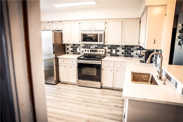 kitchen with light hardwood / wood-style floors, sink, white cabinets, stainless steel appliances, and light stone counters