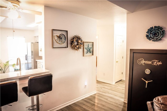 interior space featuring ceiling fan, stainless steel fridge with ice dispenser, a kitchen bar, and light hardwood / wood-style flooring