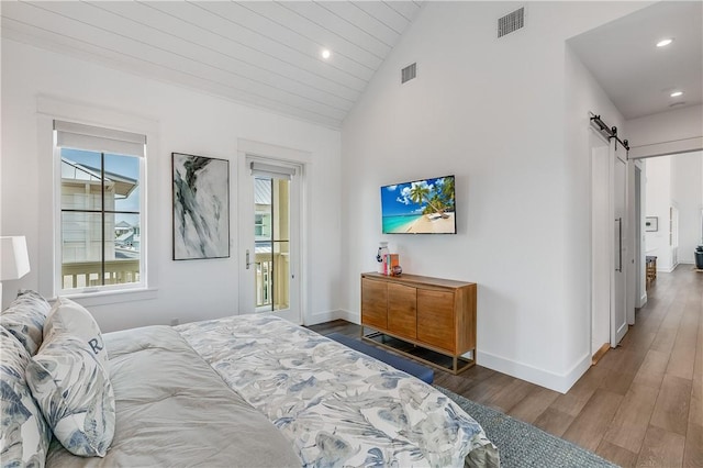 bedroom featuring a barn door, wood finished floors, lofted ceiling, baseboards, and recessed lighting