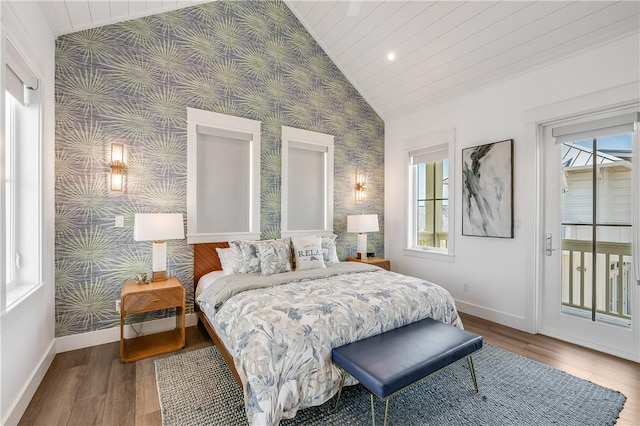 bedroom featuring wallpapered walls, lofted ceiling, baseboards, multiple windows, and wood finished floors