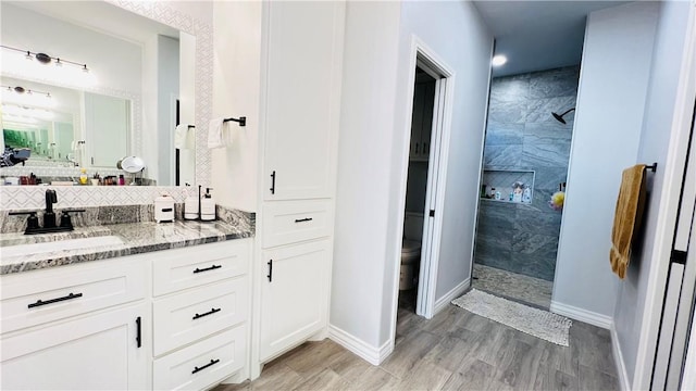 bathroom with tiled shower, vanity, toilet, and wood-type flooring