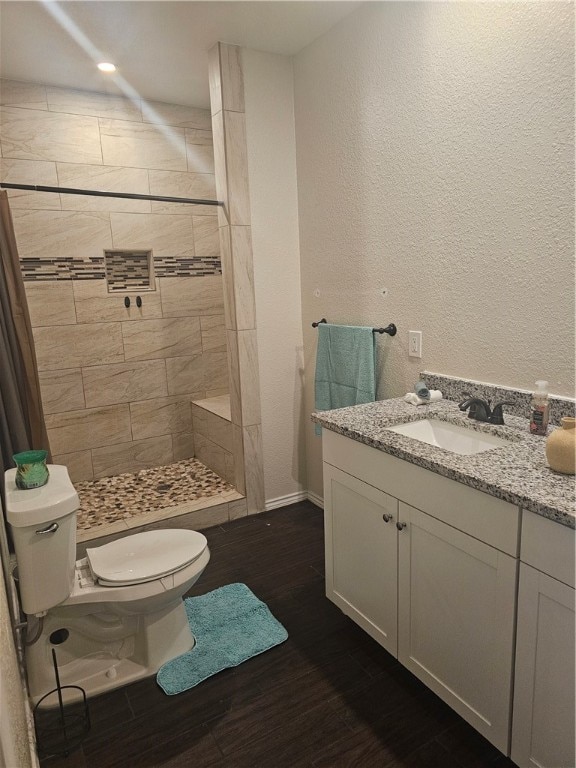 bathroom with tiled shower, hardwood / wood-style floors, vanity, and toilet