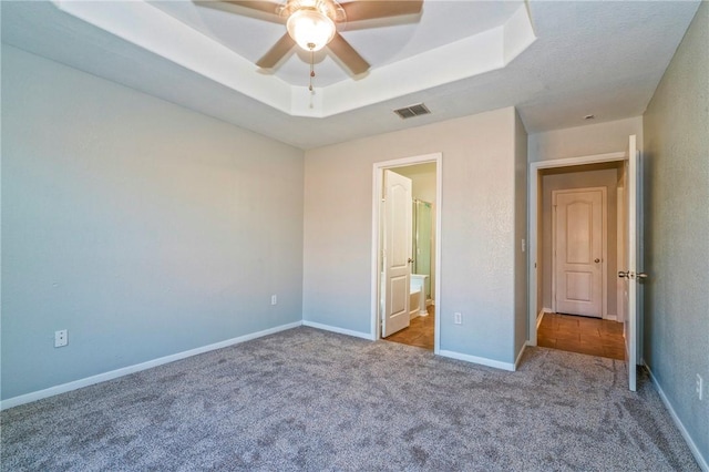 unfurnished bedroom with light carpet, ensuite bath, and a tray ceiling