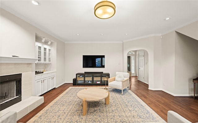 living room featuring a tiled fireplace, crown molding, and dark hardwood / wood-style flooring