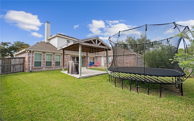 back of house featuring a patio area, a trampoline, and a lawn