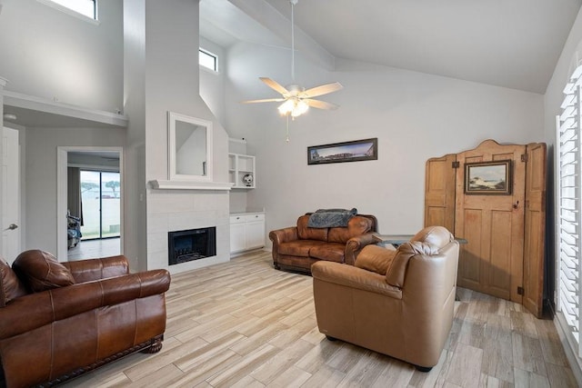 living room featuring high vaulted ceiling, light hardwood / wood-style flooring, a tile fireplace, and ceiling fan