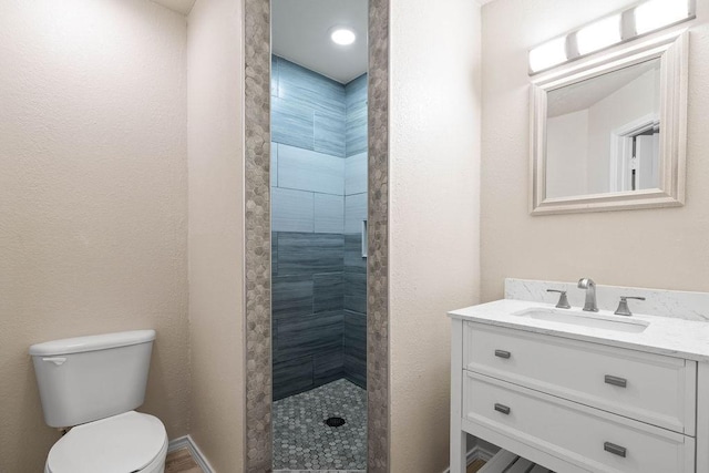 bathroom featuring vanity, a tile shower, and toilet