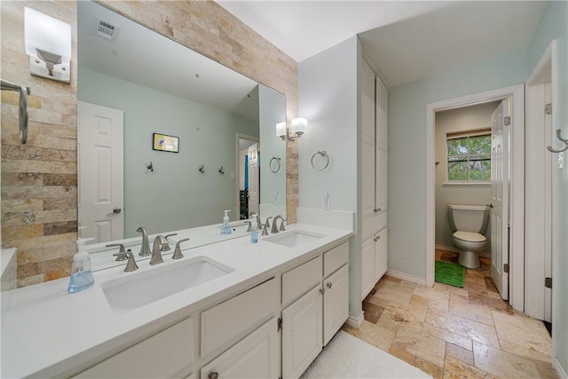 bathroom with a sink, toilet, double vanity, and stone tile floors