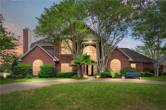 view of front of property featuring a chimney, a front lawn, and brick siding