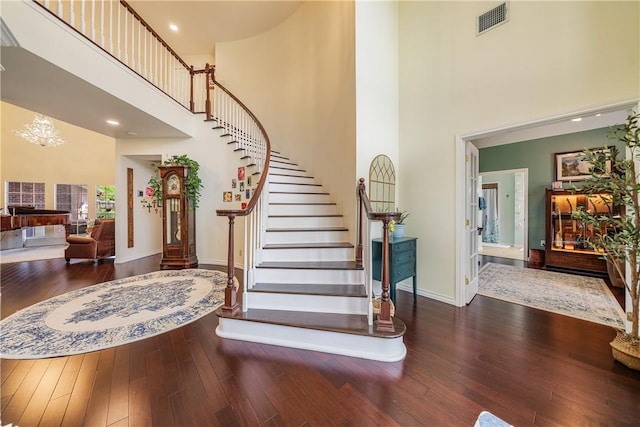 staircase with baseboards, a high ceiling, hardwood / wood-style floors, and visible vents