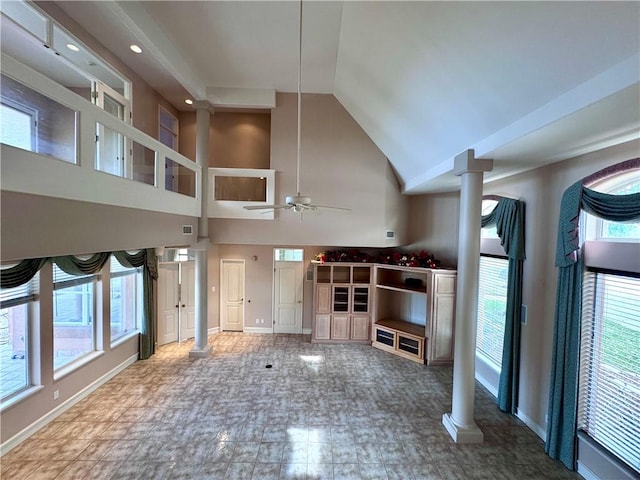 unfurnished living room with ceiling fan, decorative columns, high vaulted ceiling, and baseboards