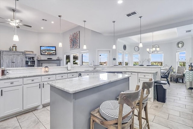 kitchen featuring visible vents, a sink, open floor plan, a center island, and white cabinets