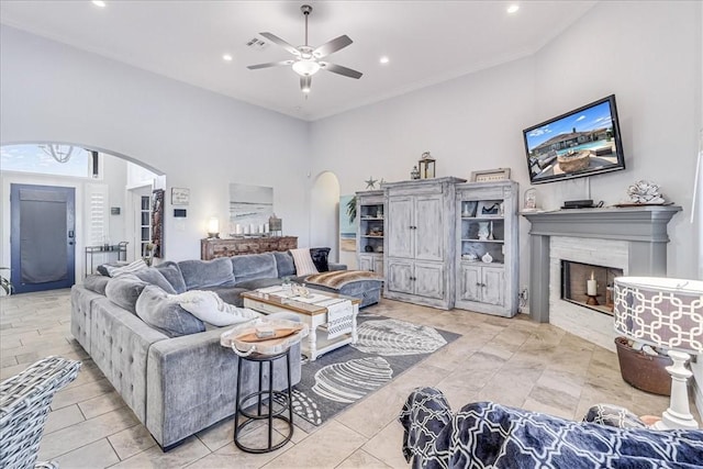 living area with arched walkways, ceiling fan, a fireplace, and a towering ceiling