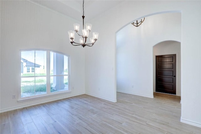 spare room with light wood-type flooring, vaulted ceiling, and a notable chandelier