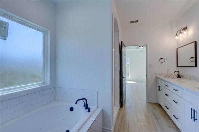 bathroom with vanity, a healthy amount of sunlight, a relaxing tiled tub, and hardwood / wood-style flooring