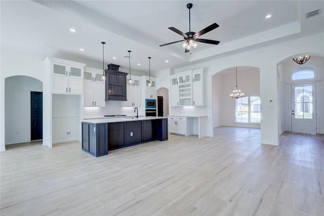 kitchen featuring a center island with sink, white cabinets, hanging light fixtures, and a tray ceiling