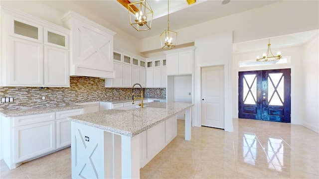 kitchen featuring light stone countertops, white cabinetry, a kitchen island with sink, and decorative backsplash