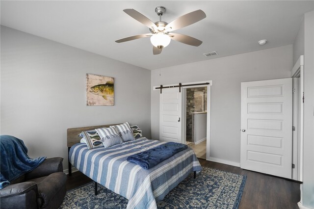 bedroom with a barn door, ceiling fan, and dark hardwood / wood-style flooring