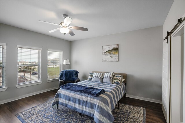 bedroom featuring dark wood-type flooring, a barn door, and ceiling fan