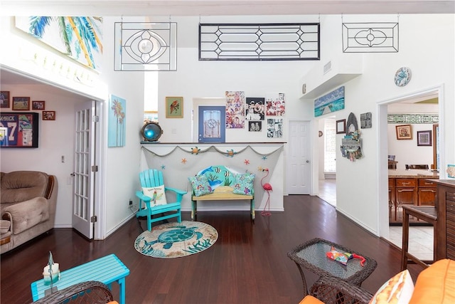 living room with wood finished floors, visible vents, baseboards, a towering ceiling, and french doors