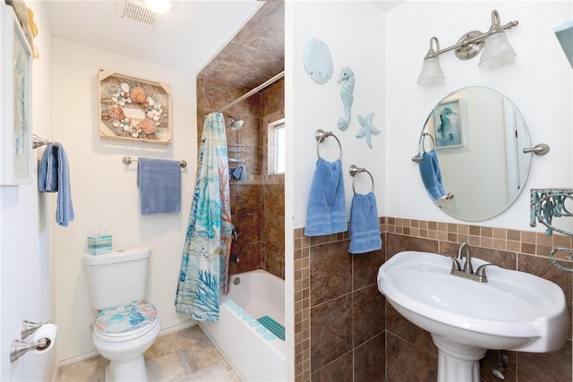 bathroom featuring a sink, baseboards, shower / bath combo with shower curtain, toilet, and tile walls