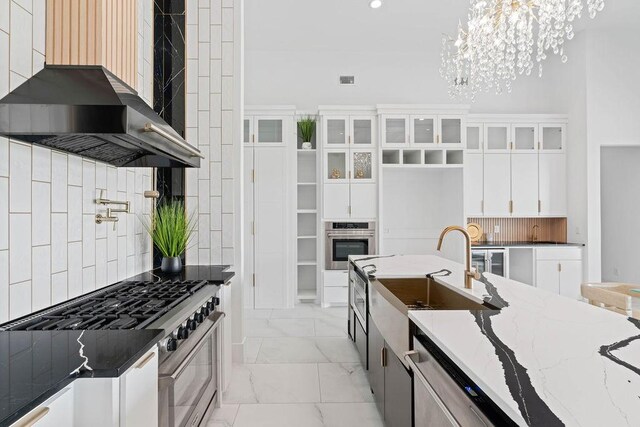 5402 Bonanza Dr, Corpus Christi, TX 78414 - kitchen with appliances with stainless steel finishes, a chandelier, wall chimney exhaust hood, light marble finish flooring, and white cabinets