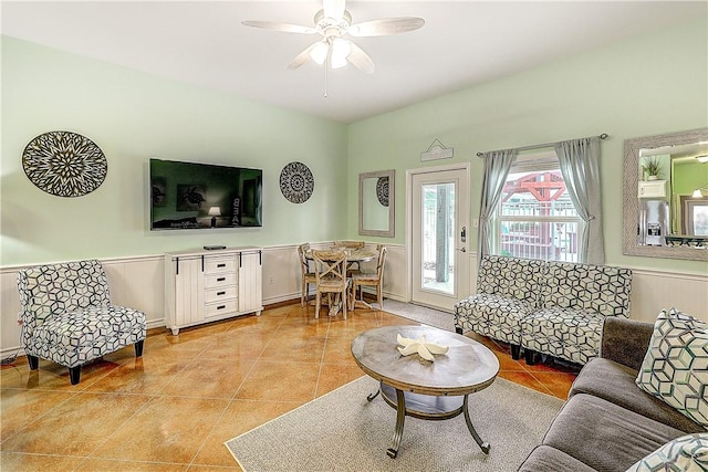 living room with a wainscoted wall, a ceiling fan, and light tile patterned flooring