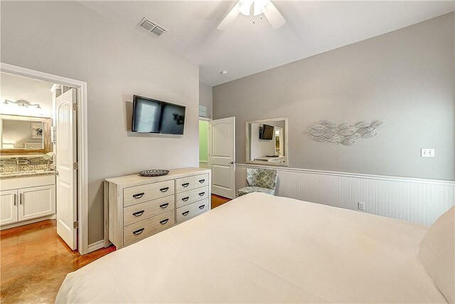 bedroom featuring concrete flooring, ceiling fan, wainscoting, ensuite bath, and visible vents