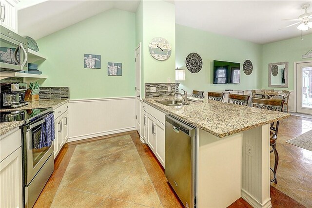 kitchen with a peninsula, a kitchen breakfast bar, light stone counters, a sink, and appliances with stainless steel finishes