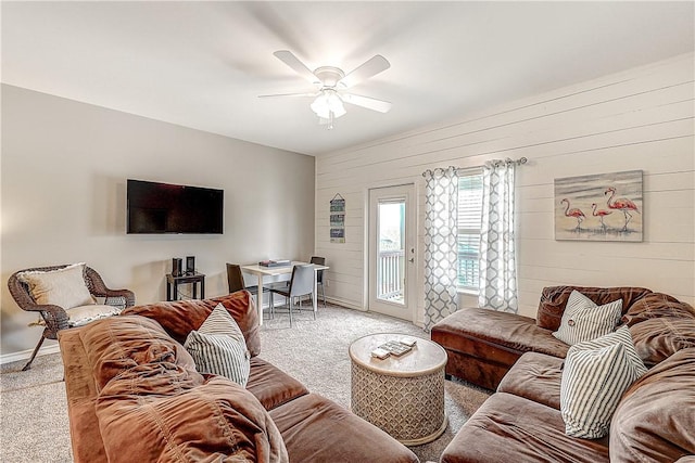 living room featuring baseboards, a ceiling fan, wood walls, and light colored carpet