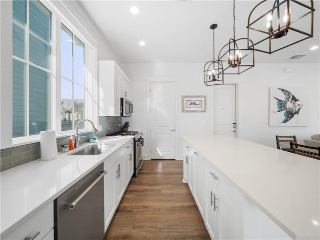 kitchen with dark wood finished floors, a sink, decorative backsplash, stainless steel appliances, and a chandelier