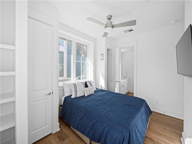 bedroom featuring visible vents, baseboards, ensuite bathroom, wood finished floors, and a ceiling fan