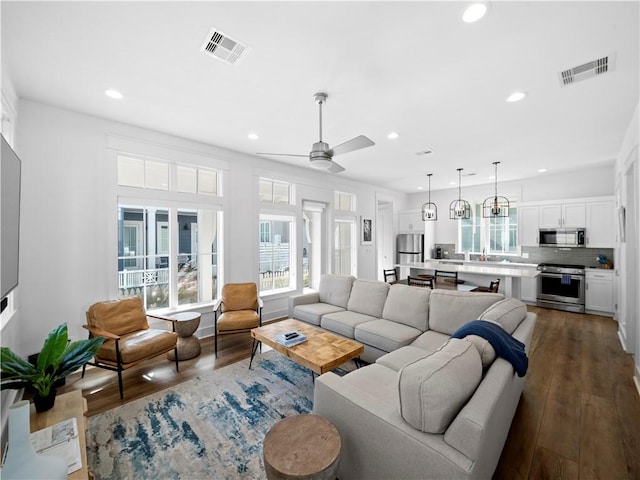 living room featuring a ceiling fan, visible vents, and dark wood-style flooring