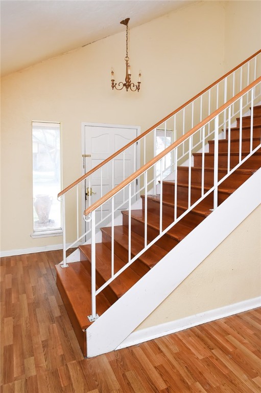 stairway with high vaulted ceiling, hardwood / wood-style flooring, and an inviting chandelier