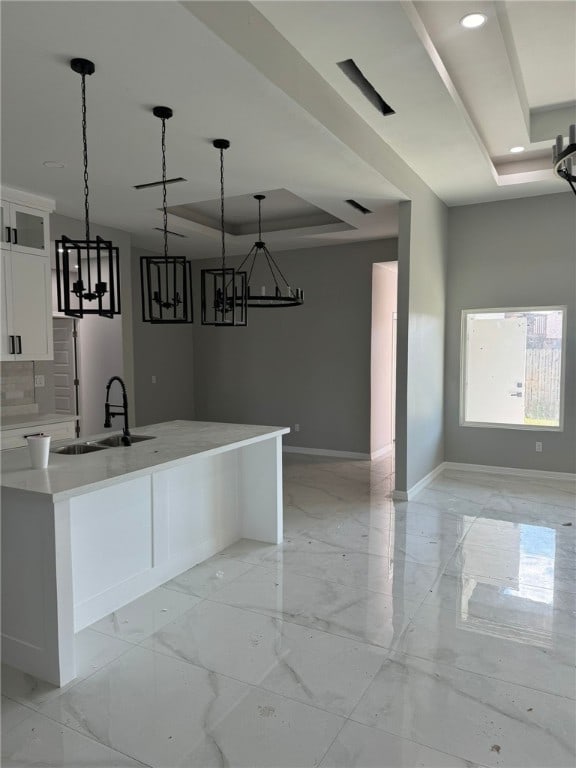 kitchen featuring a tray ceiling, white cabinetry, sink, and hanging light fixtures