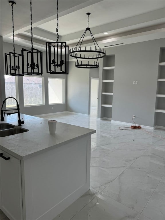 kitchen with sink, built in features, decorative light fixtures, light stone counters, and white cabinetry