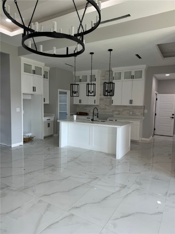 kitchen featuring white cabinets, decorative light fixtures, a chandelier, and an island with sink