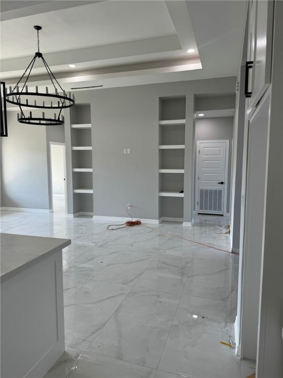 unfurnished dining area featuring built in shelves, a tray ceiling, and a notable chandelier