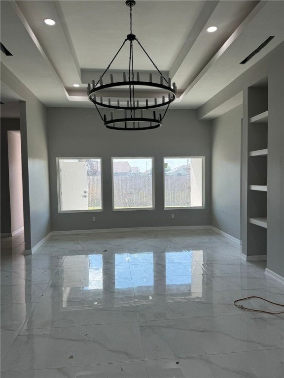 unfurnished dining area featuring a chandelier, a raised ceiling, and built in features