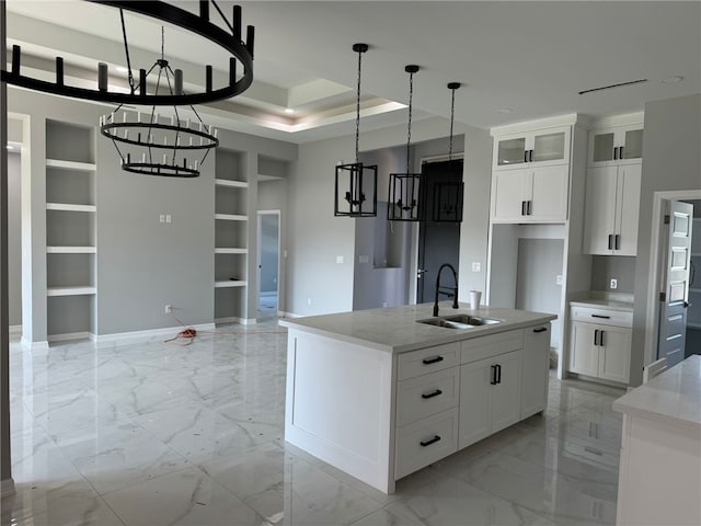 kitchen with sink, built in features, a tray ceiling, a center island with sink, and white cabinets