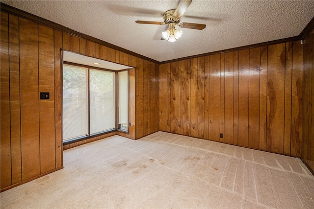 carpeted spare room featuring ornamental molding, wooden walls, a textured ceiling, and ceiling fan