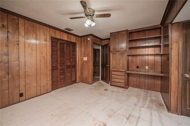 unfurnished bedroom with wood walls, light carpet, ceiling fan, a textured ceiling, and a closet