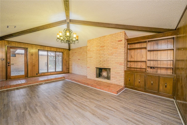 unfurnished living room featuring a fireplace, wood-type flooring, wooden walls, and an inviting chandelier