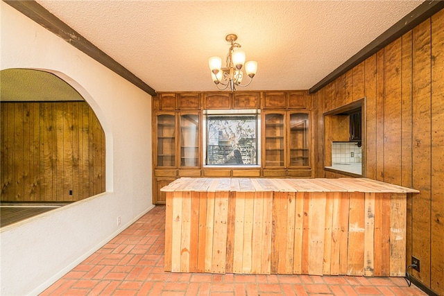 bar featuring wood walls, a textured ceiling, pendant lighting, and a notable chandelier